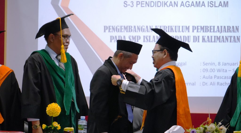 Rektor UIN Antasari saat mengalungkan selempang titel baru untuk Dr. H. Khairani, M.Pd.I. (Foto:Humas/Hadi Rustami)