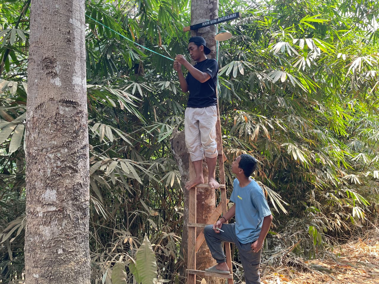 Kelompok 20 Mahasiswa KKN UIN Antasari memasang plang lampu penerangan di akses menuju sungai di Dusun Pinai, Selasa, 29 September 2026.